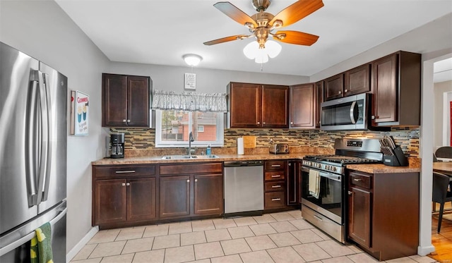 kitchen featuring ceiling fan, stainless steel appliances, a sink, dark brown cabinets, and decorative backsplash