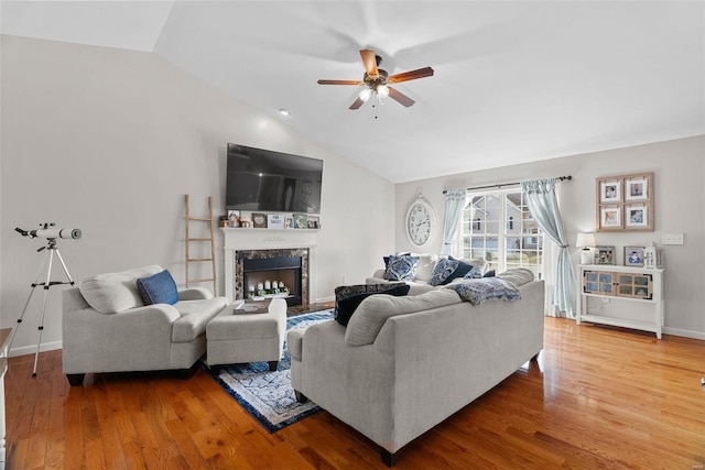 living area featuring baseboards, ceiling fan, a premium fireplace, wood finished floors, and vaulted ceiling