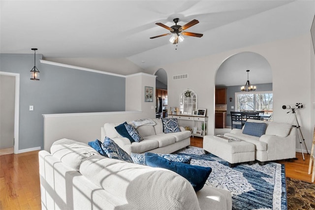 living room with visible vents, arched walkways, wood finished floors, vaulted ceiling, and ceiling fan with notable chandelier