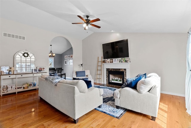 living room featuring lofted ceiling, visible vents, arched walkways, and wood finished floors