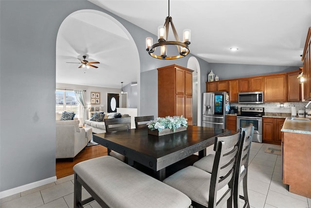 dining room featuring light tile patterned floors, baseboards, arched walkways, vaulted ceiling, and ceiling fan with notable chandelier