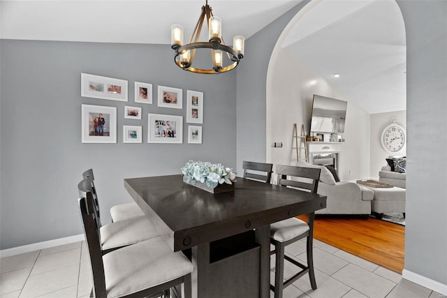 dining area with arched walkways, light tile patterned floors, lofted ceiling, and baseboards