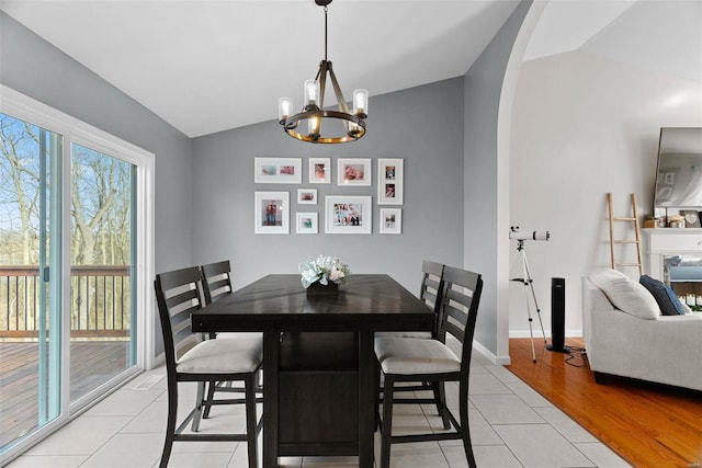 dining space featuring a chandelier, arched walkways, vaulted ceiling, and light tile patterned floors