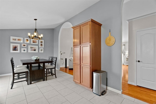 dining room featuring arched walkways, vaulted ceiling, baseboards, and light tile patterned floors