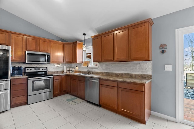 kitchen with stainless steel appliances, a sink, vaulted ceiling, brown cabinets, and tasteful backsplash