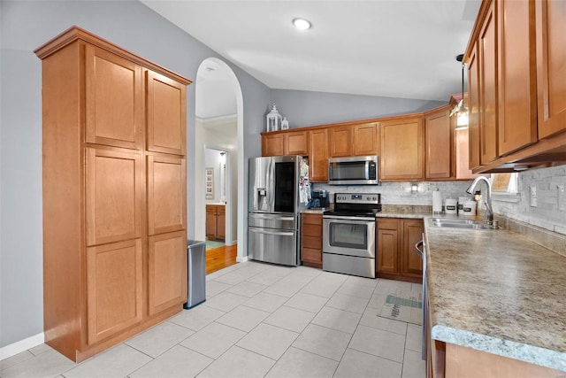 kitchen featuring light tile patterned floors, a sink, vaulted ceiling, appliances with stainless steel finishes, and tasteful backsplash