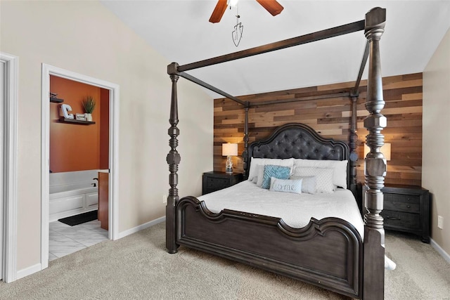 bedroom with wooden walls, baseboards, a ceiling fan, light colored carpet, and ensuite bath