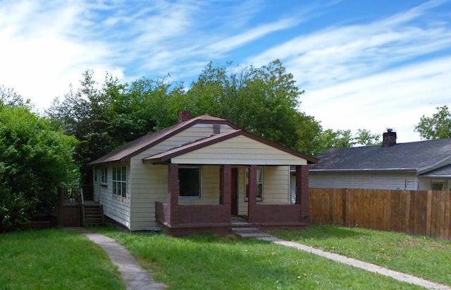 bungalow-style house with covered porch, fence, and a front lawn