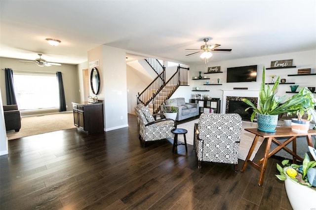 living area with stairs, dark wood-type flooring, a high end fireplace, and a ceiling fan