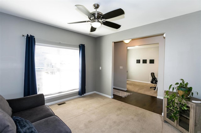 living area featuring carpet floors, baseboards, visible vents, and ceiling fan