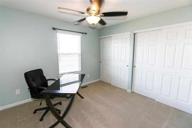 home office featuring baseboards, ceiling fan, visible vents, and light colored carpet