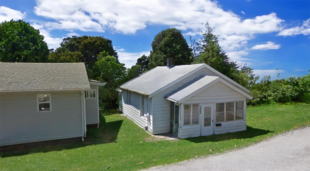 view of front of property featuring a shingled roof, a sunroom, and a front lawn