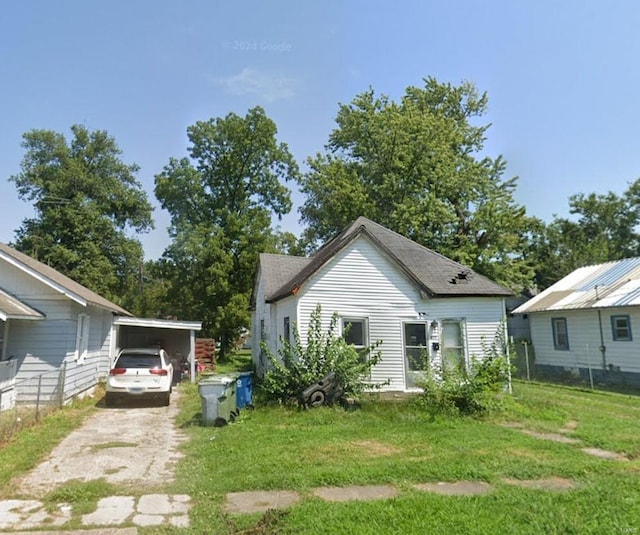 rear view of house with dirt driveway, fence, a carport, and a yard