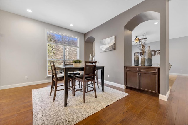 dining space with hardwood / wood-style flooring, baseboards, and arched walkways