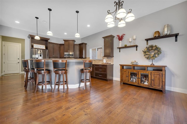 kitchen with dark wood-style floors, a breakfast bar, dark brown cabinets, appliances with stainless steel finishes, and a center island