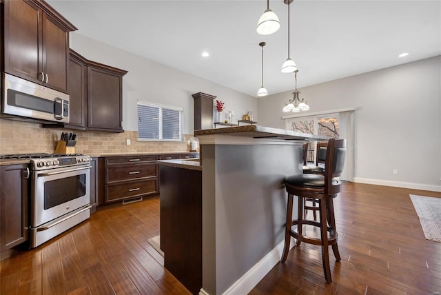 kitchen featuring dark brown cabinets, decorative backsplash, a breakfast bar area, and stainless steel appliances