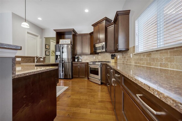 kitchen featuring light stone counters, wood finished floors, dark brown cabinetry, appliances with stainless steel finishes, and tasteful backsplash