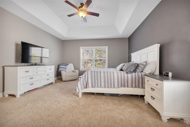 bedroom with light carpet, ceiling fan, baseboards, and a tray ceiling