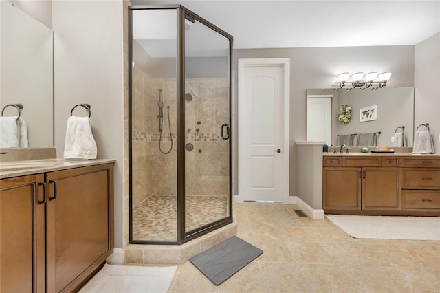 bathroom featuring a shower stall, two vanities, baseboards, and a sink