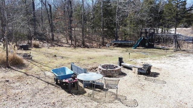 view of yard featuring a trampoline, a playground, a fire pit, and a view of trees