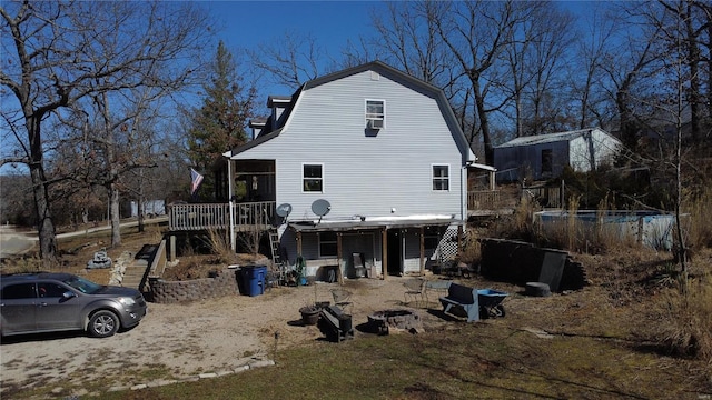 back of property with a fire pit, a wooden deck, a gambrel roof, and stairs