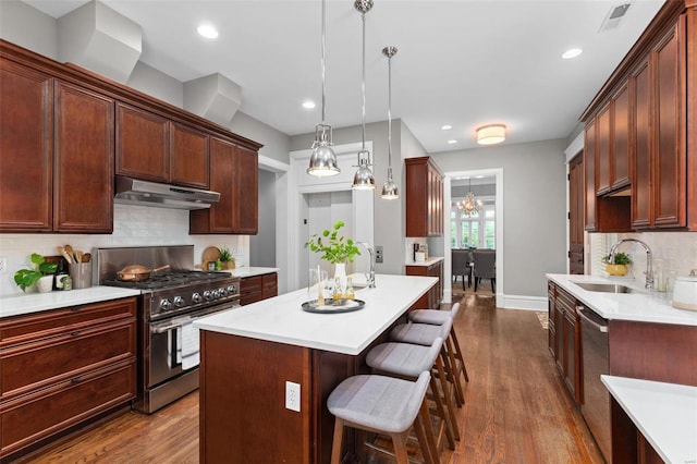 kitchen with under cabinet range hood, stainless steel appliances, a breakfast bar, a sink, and visible vents