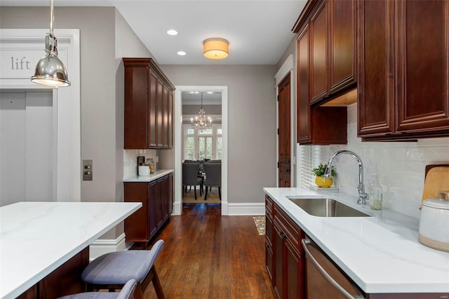 kitchen featuring light stone counters, hanging light fixtures, dark wood-type flooring, a sink, and dishwasher