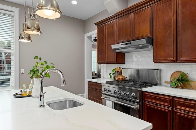 kitchen with tasteful backsplash, decorative light fixtures, stainless steel stove, under cabinet range hood, and a sink