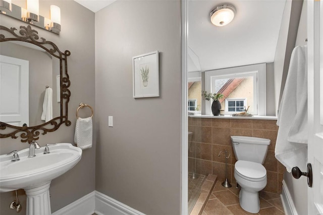 bathroom with toilet, tile patterned flooring, tile walls, and a sink