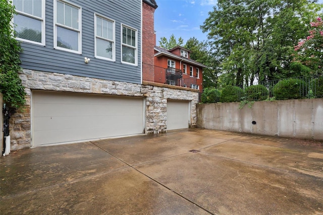 view of property exterior with a garage, stone siding, fence, and driveway