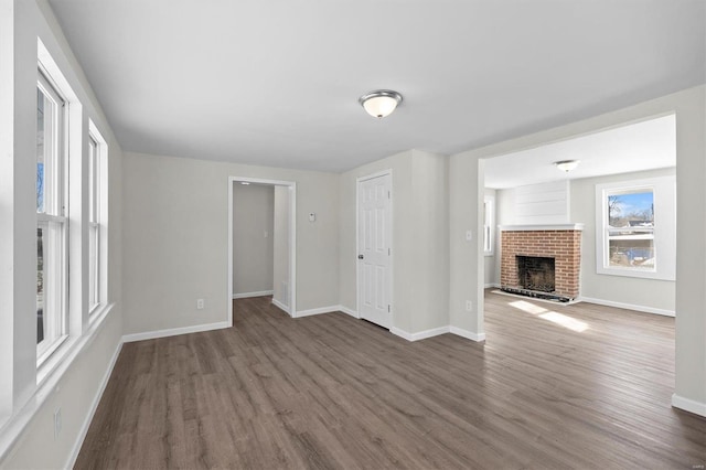 unfurnished living room featuring a brick fireplace, wood finished floors, and baseboards