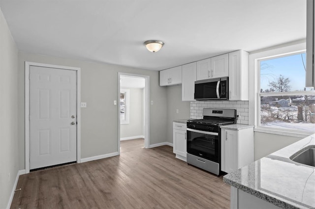 kitchen featuring baseboards, white cabinets, appliances with stainless steel finishes, backsplash, and light wood finished floors