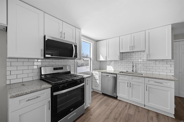 kitchen featuring backsplash, appliances with stainless steel finishes, white cabinets, a sink, and wood finished floors