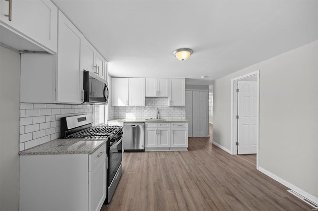 kitchen featuring stainless steel appliances, backsplash, white cabinetry, a sink, and wood finished floors