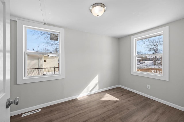 spare room featuring wood finished floors, visible vents, and baseboards