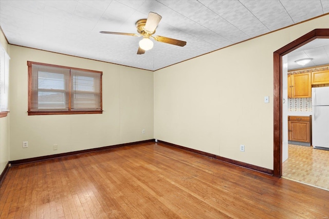 spare room featuring light wood-style flooring, baseboards, a ceiling fan, and ornamental molding