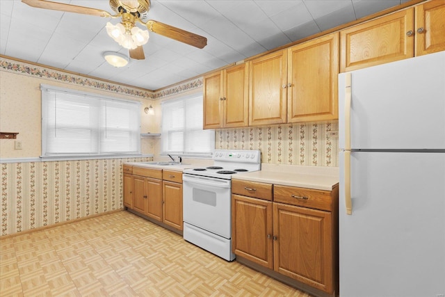 kitchen with light countertops, ceiling fan, a sink, white appliances, and wallpapered walls