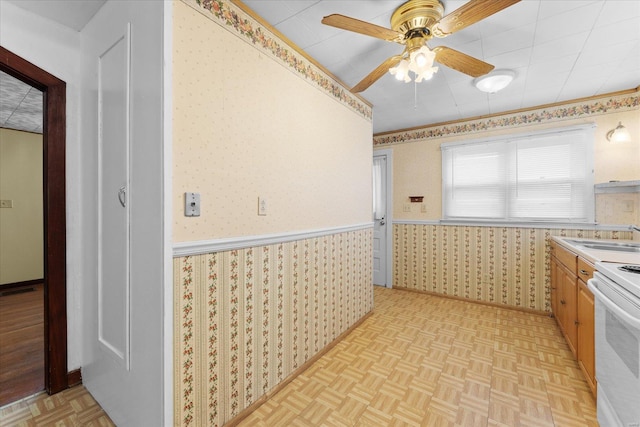 kitchen featuring ceiling fan, a wainscoted wall, a sink, white electric range oven, and wallpapered walls