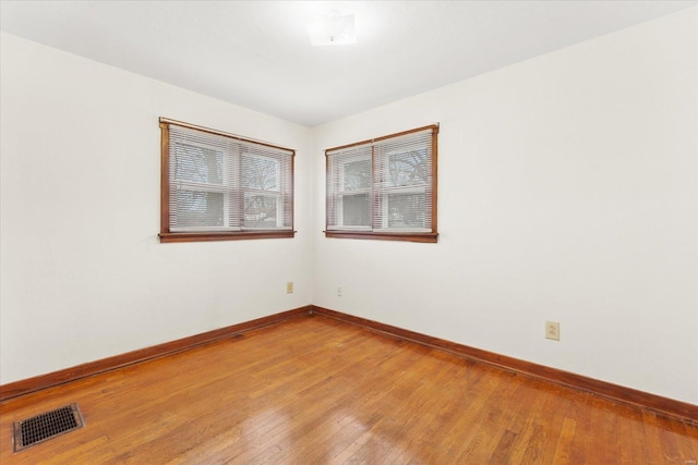 spare room with wood-type flooring, visible vents, and baseboards