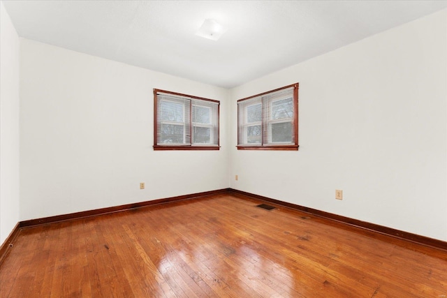 spare room with hardwood / wood-style floors, visible vents, and baseboards