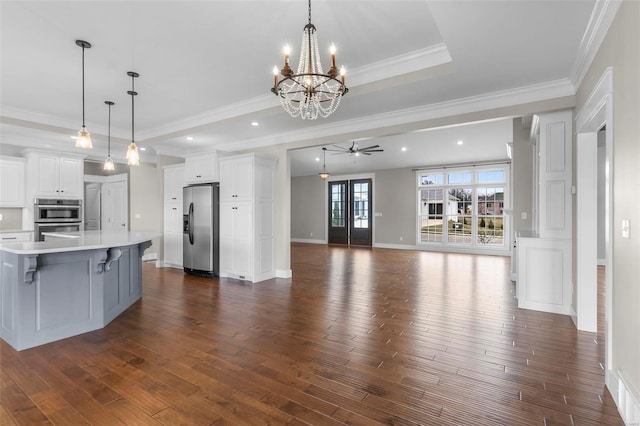 kitchen featuring stainless steel appliances, dark wood-style flooring, open floor plan, light countertops, and a tray ceiling