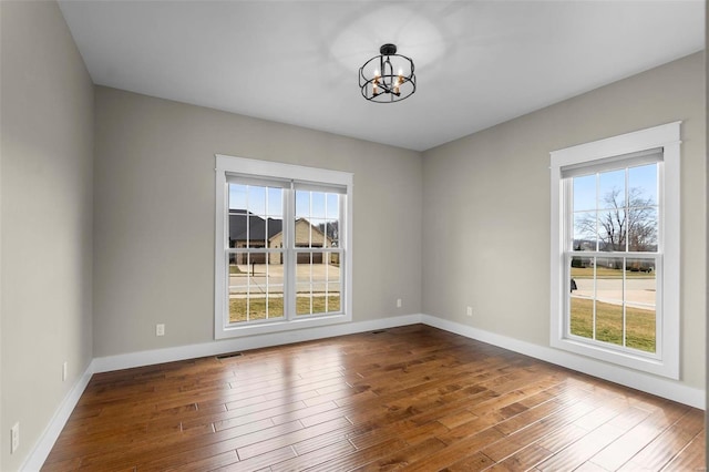 unfurnished room featuring plenty of natural light, visible vents, and dark wood finished floors