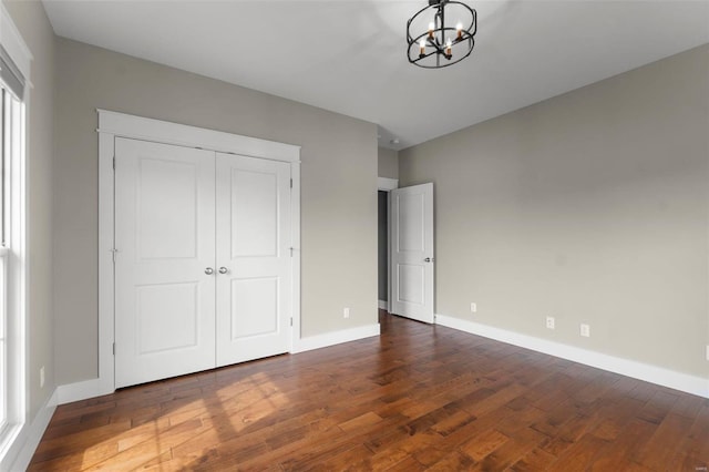 unfurnished bedroom with dark wood-style floors, a closet, a notable chandelier, and baseboards