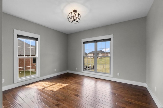 spare room featuring a notable chandelier, dark wood-style flooring, visible vents, and baseboards