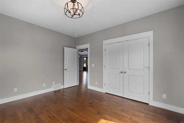 unfurnished bedroom featuring dark wood-style flooring, a closet, visible vents, an inviting chandelier, and baseboards