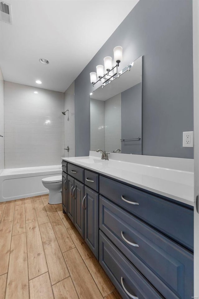 bathroom featuring visible vents, toilet, vanity, shower / tub combination, and wood finished floors