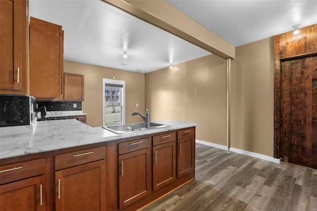 kitchen with a peninsula, dark wood-type flooring, a sink, backsplash, and brown cabinetry