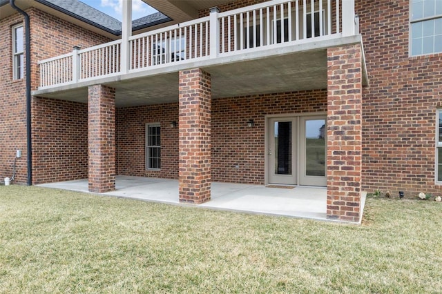 rear view of property featuring a patio, brick siding, a lawn, and a balcony