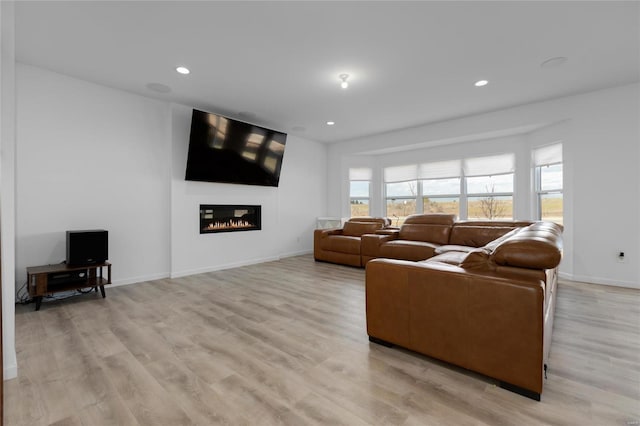 living area featuring a glass covered fireplace, light wood-style flooring, recessed lighting, and baseboards