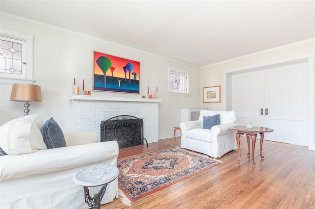 living area with wood finished floors, a brick fireplace, and ornamental molding